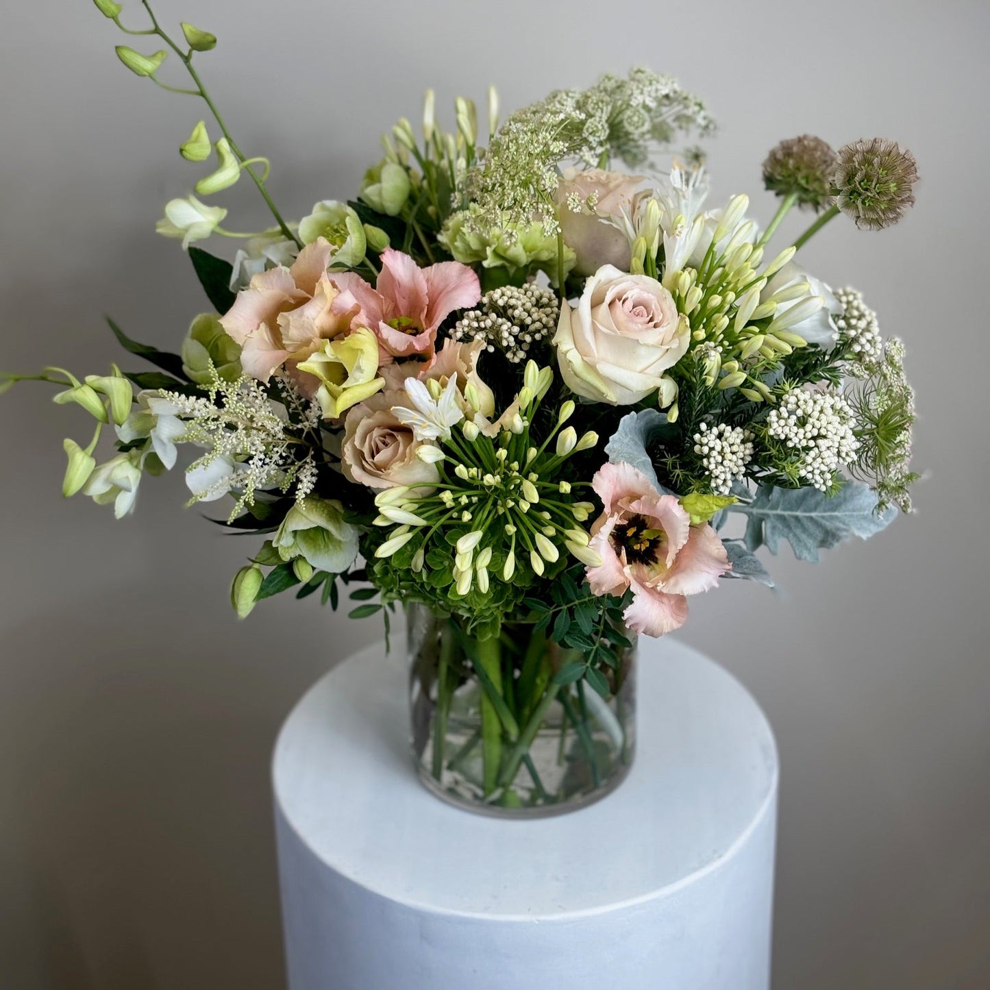 Bouquet of flowers in a clear vase on a white pedestal against a gray background