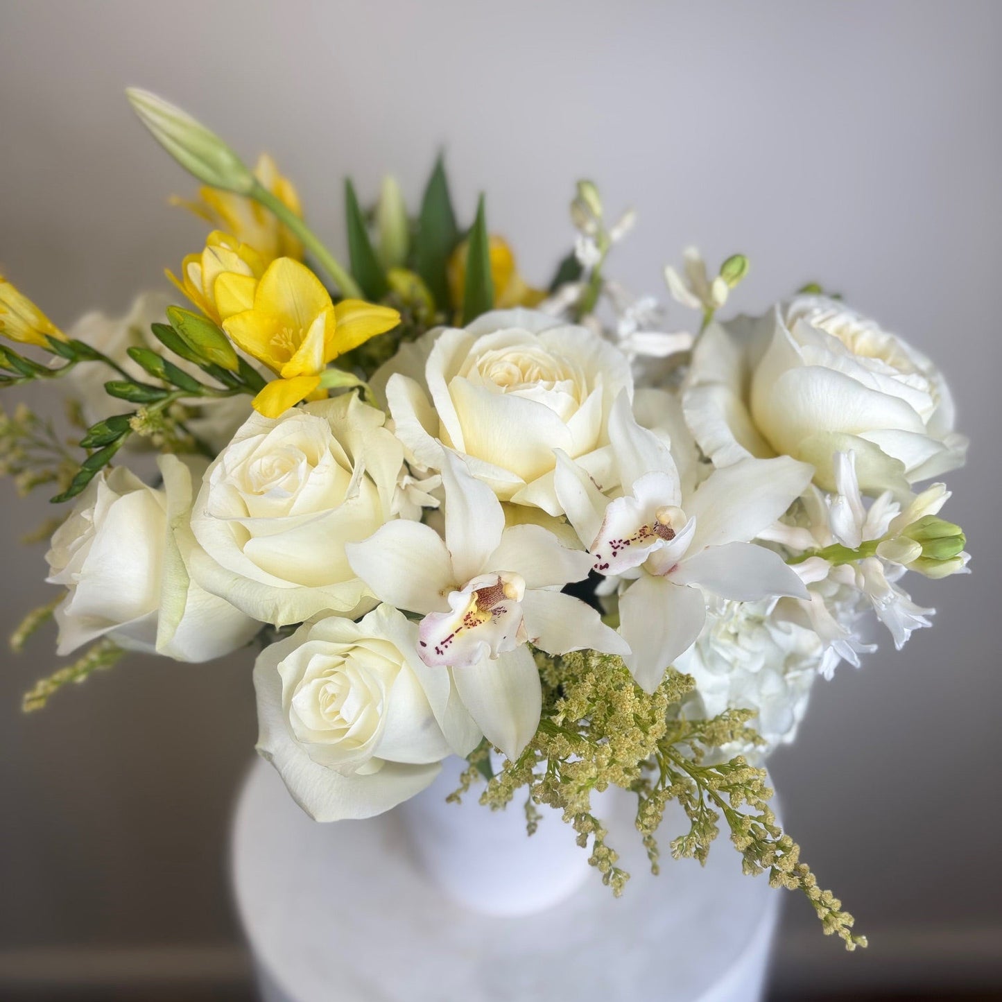 Floral arrangement with white and yellow flowers in a white vase on a neutral background