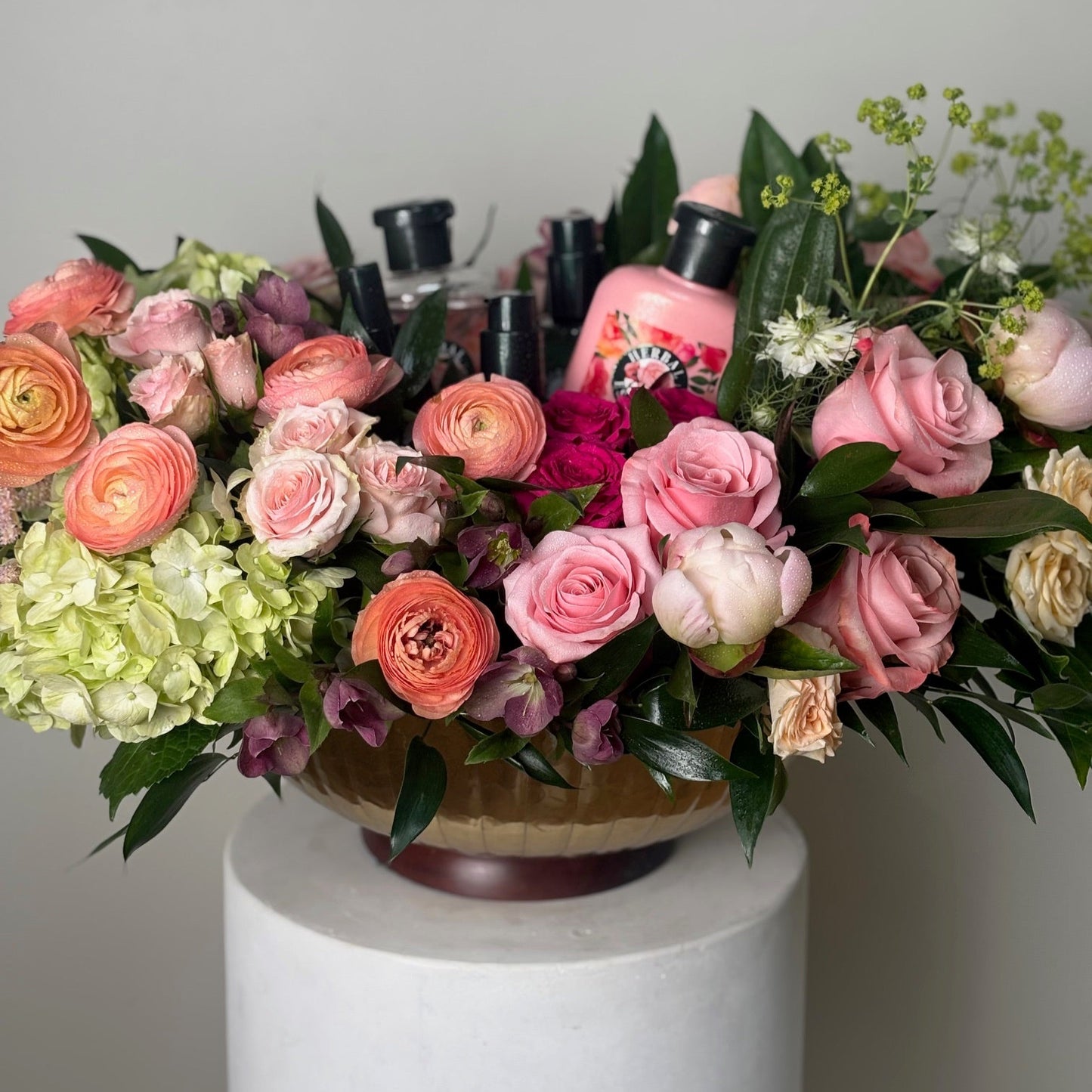 Bouquet of flowers with a pink bottle in the center on a white pedestal against a gray background