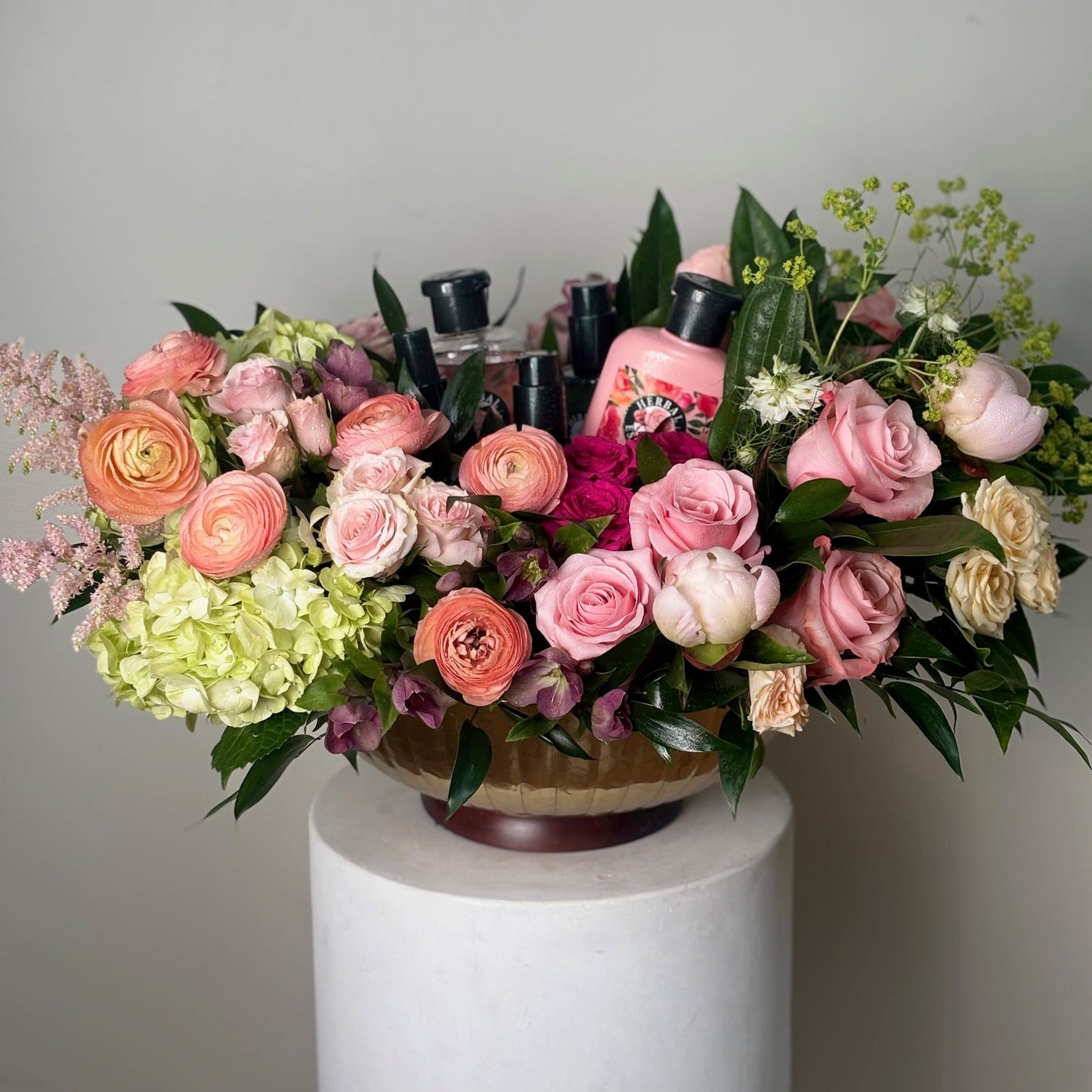 Bouquet of flowers with a bottle of pink wine on a white pedestal against a gray background