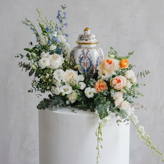 Funeral urn with flowers on a white pedestal against a gray background