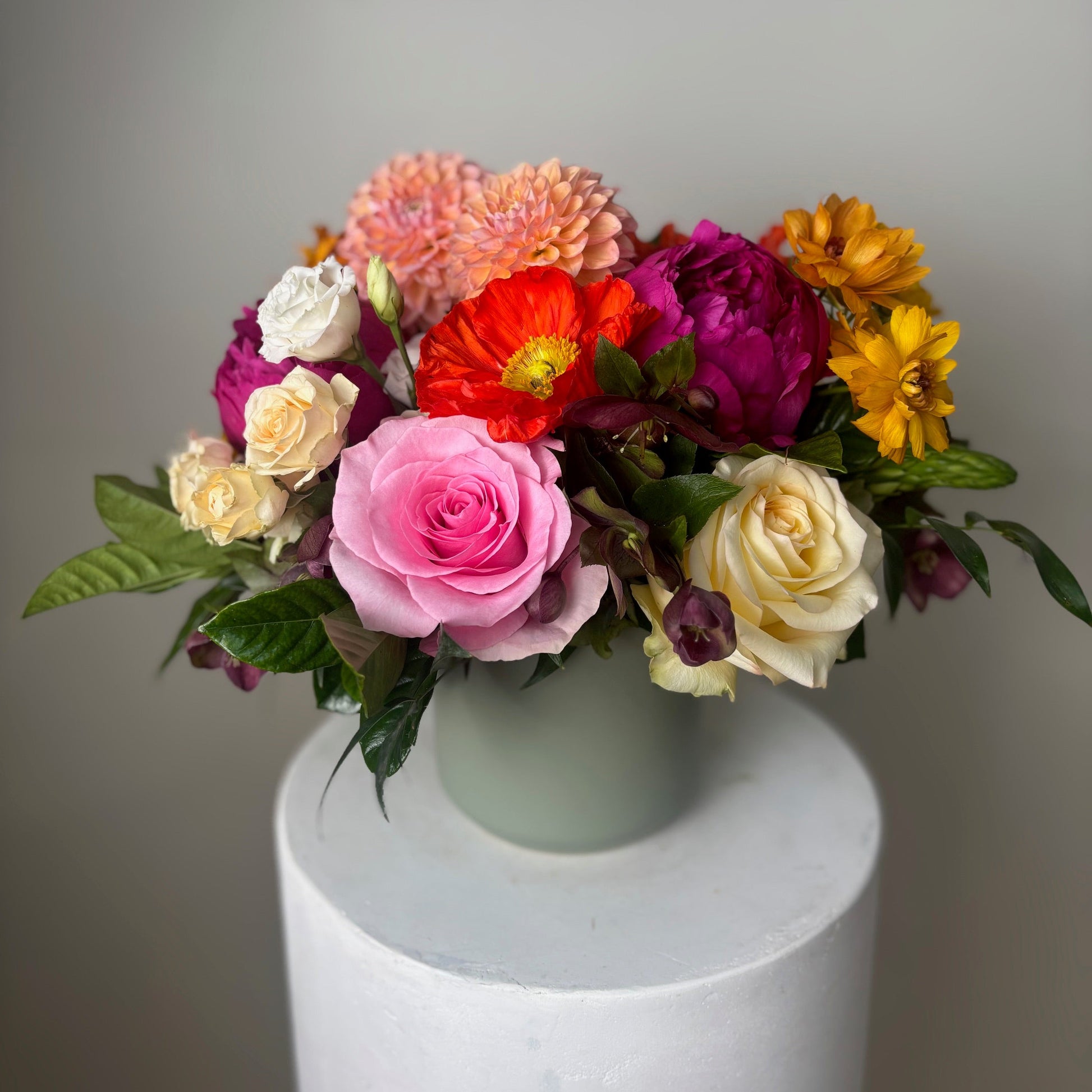 Colorful flower arrangement in a vase on a white pedestal against a gray background