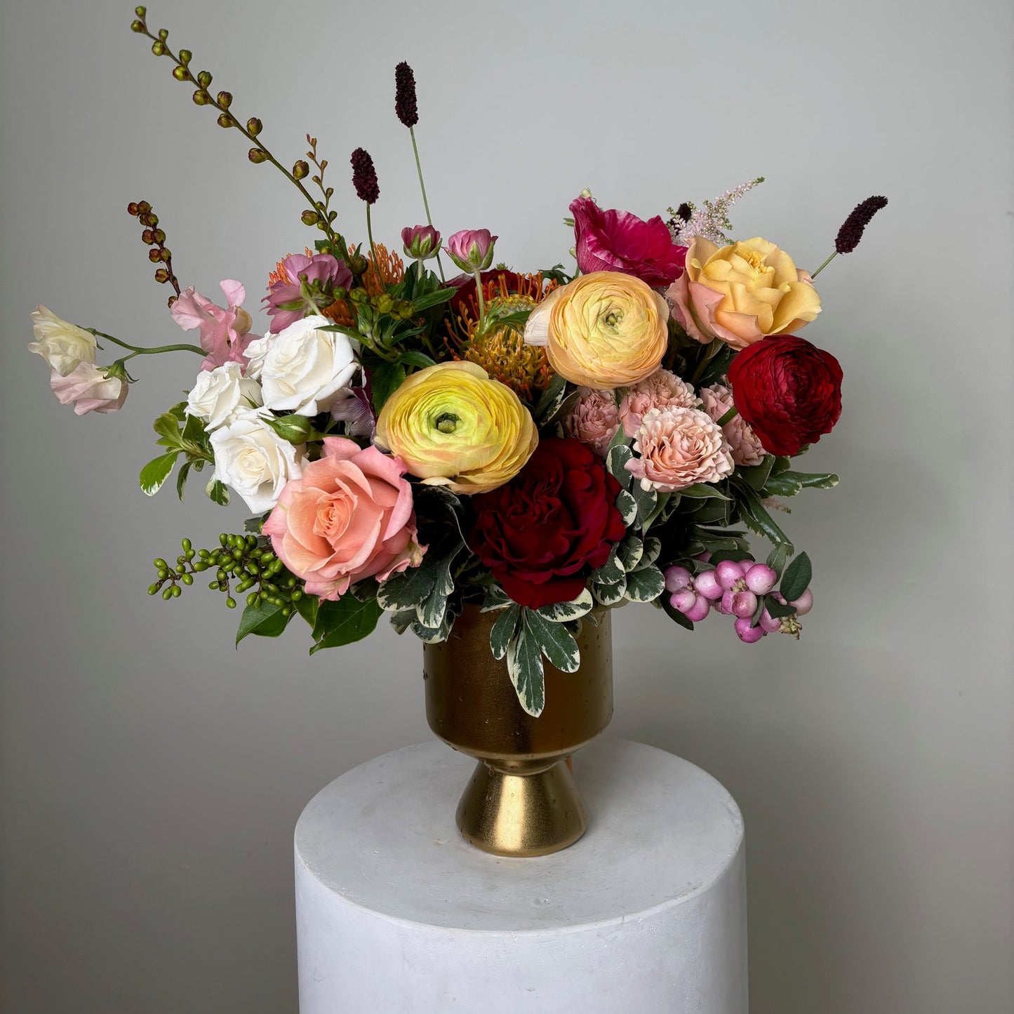 Colorful flower arrangement on a white pedestal with a gold wick against a gray background