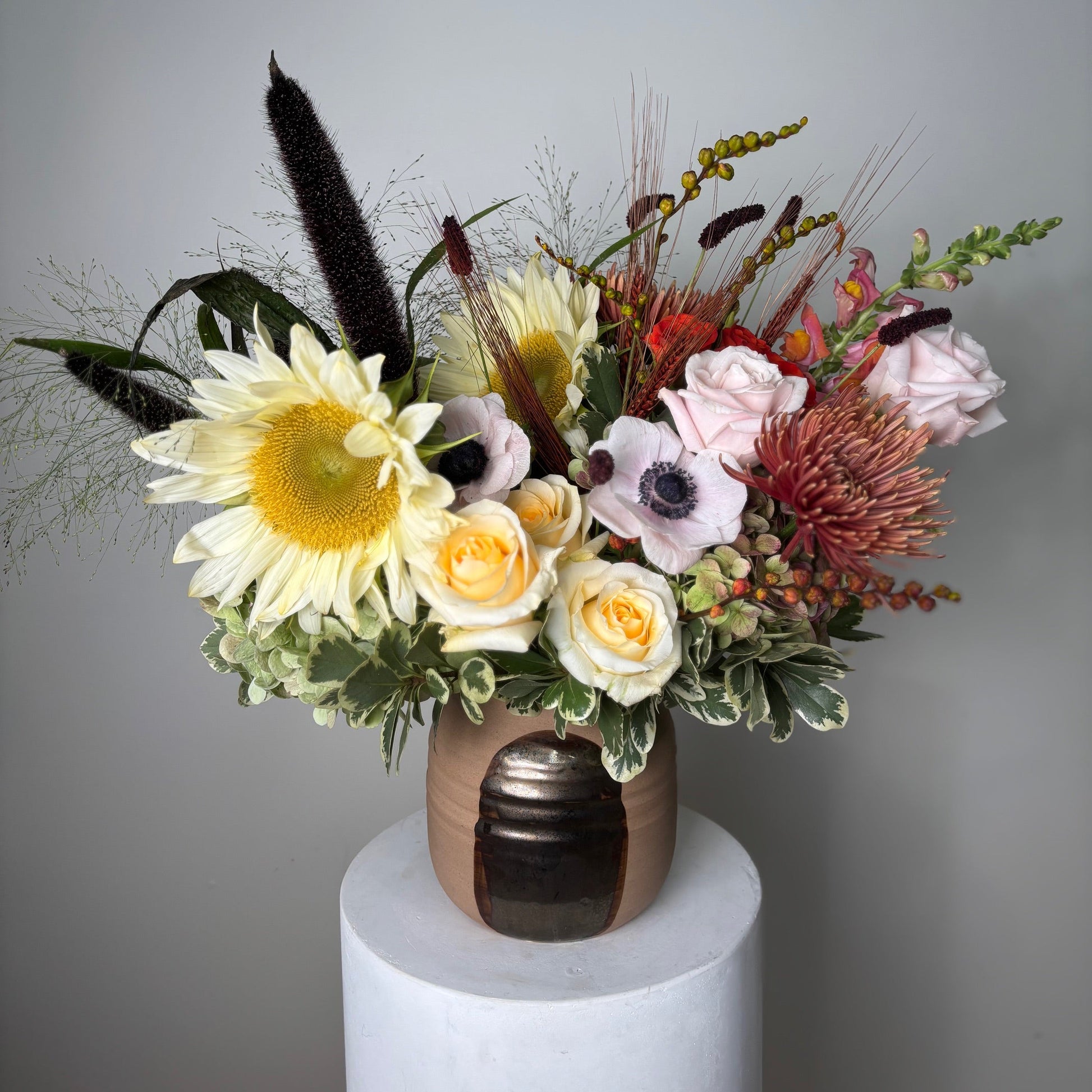 Floral arrangement in a bronze vase on a white pedestal against a gray background