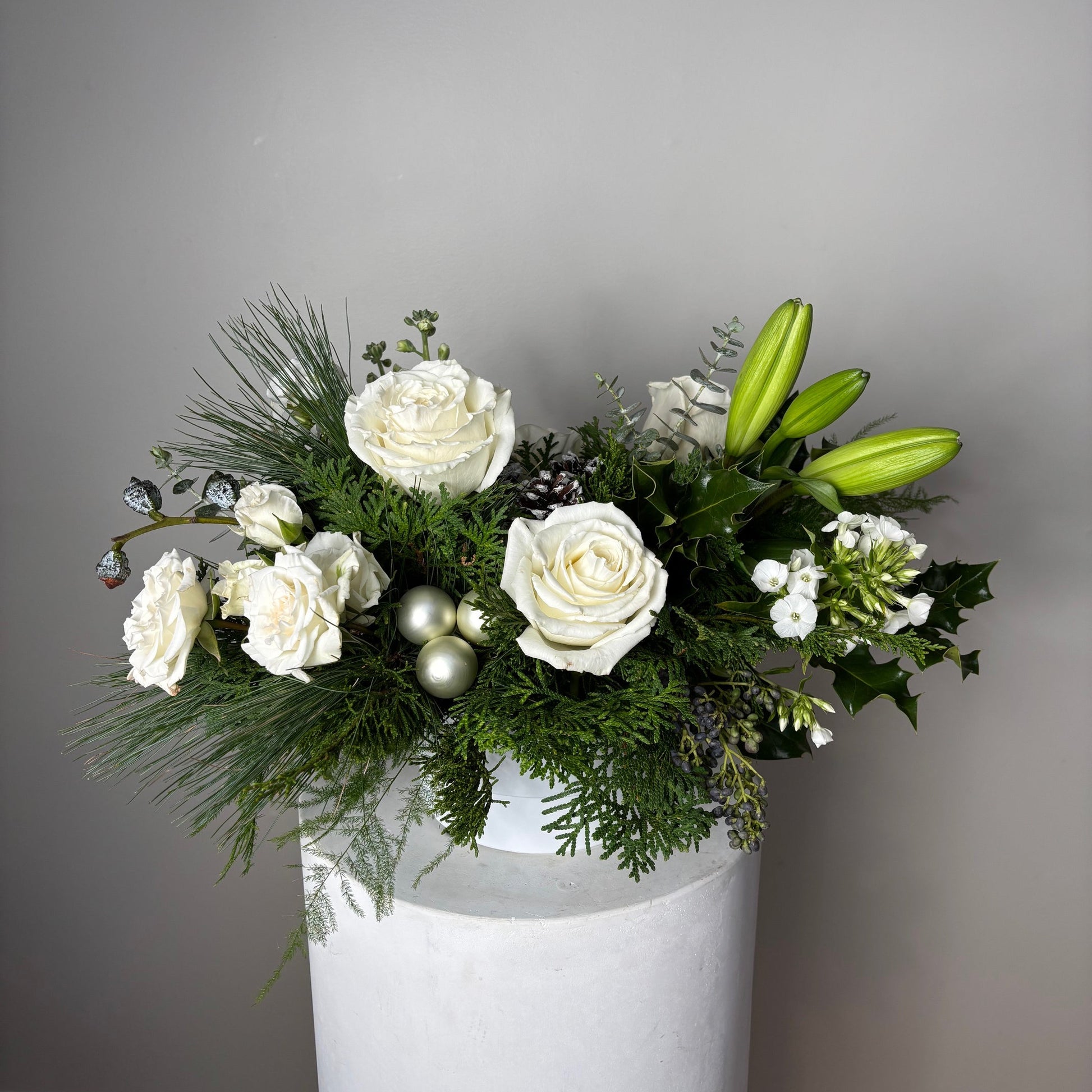 Floral arrangement with white flowers and winter greenery on a plain background