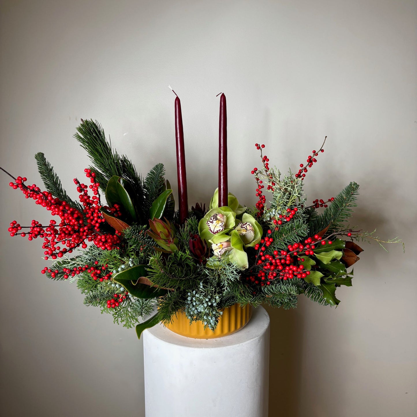 Decorative floral arrangement with greenery and red berries on a white surface.