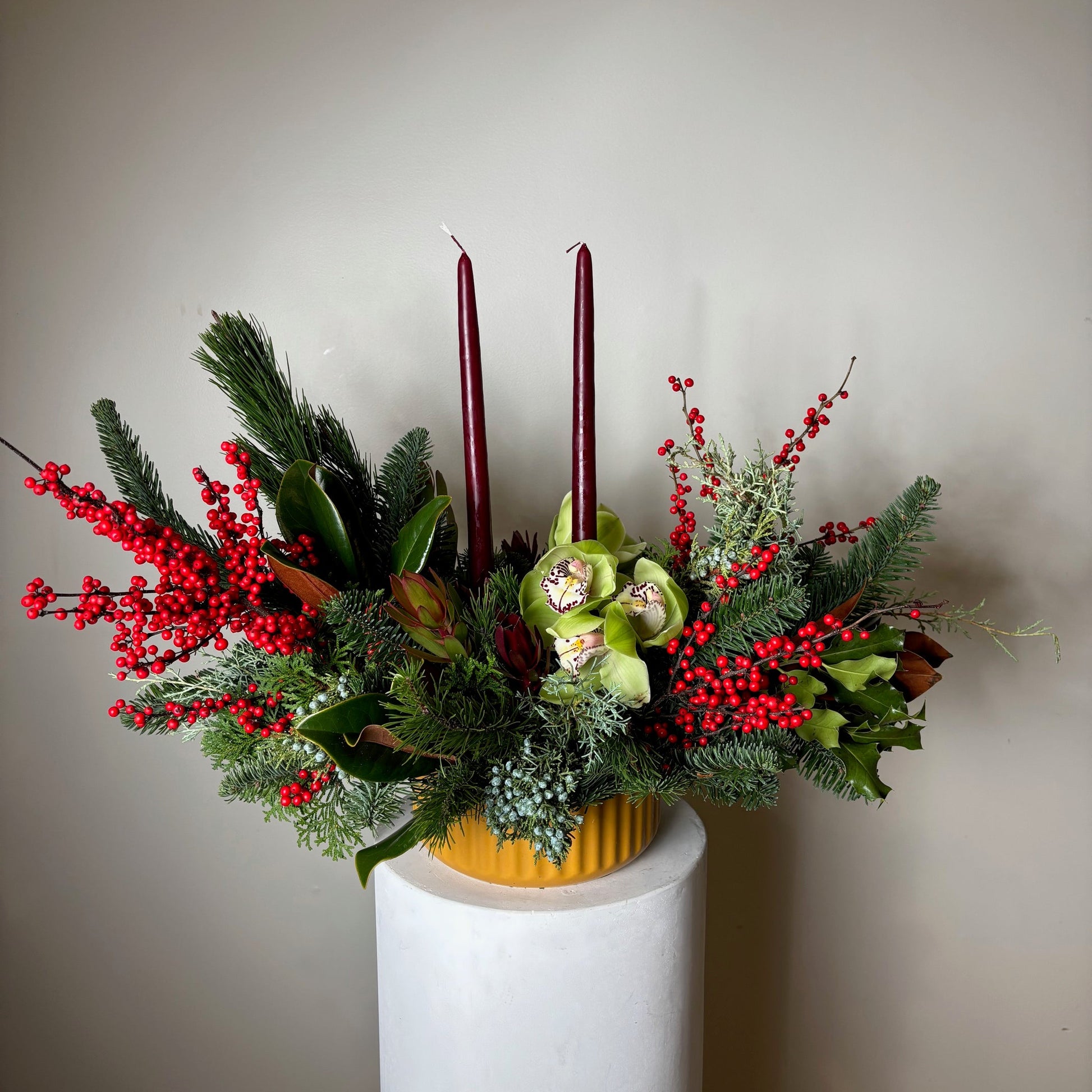 Decorative floral arrangement with greenery and red berries on a white surface.