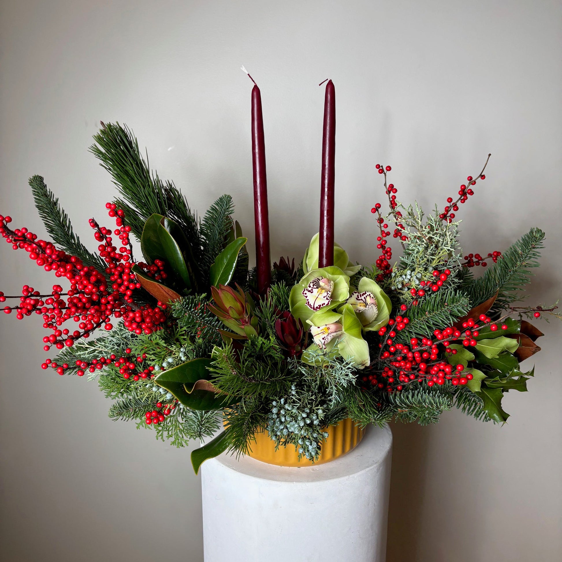 Decorative floral arrangement with greenery and red berries on a white surface.