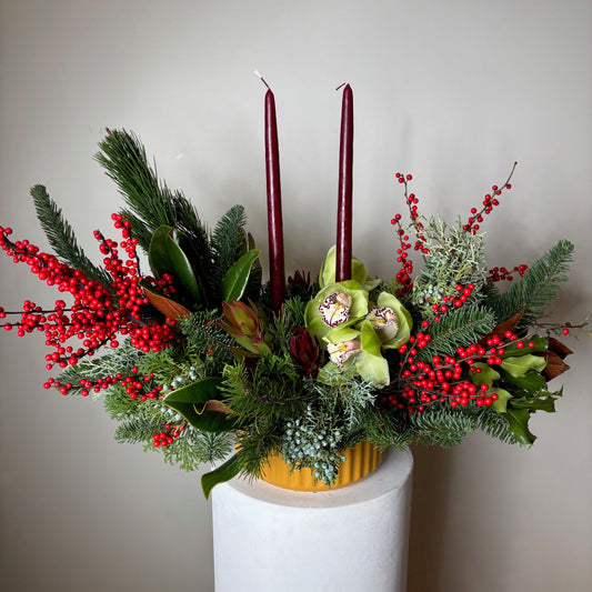 Decorative floral arrangement with greenery and red berries on a white surface.