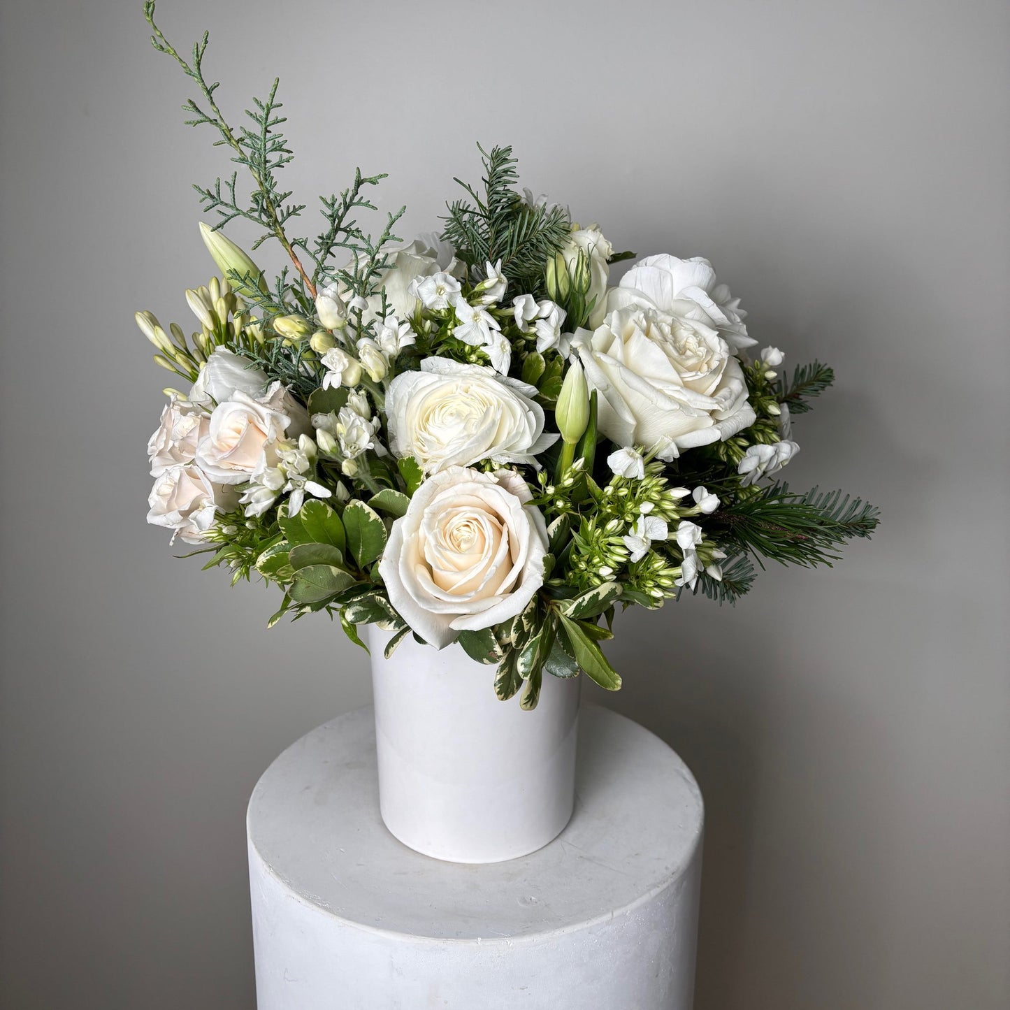Bouquet of white flowers with greenery in a cylindrical white container on a gray background