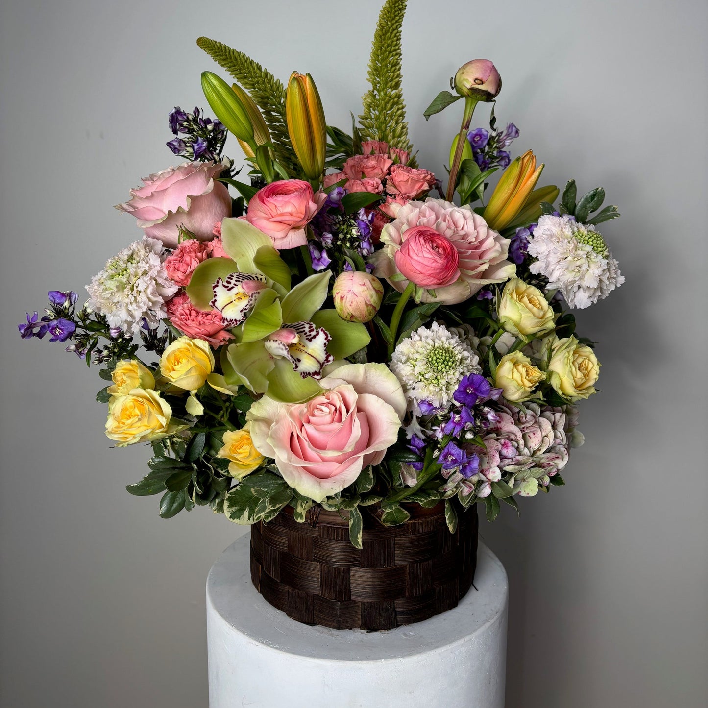 Colorful flower arrangement in a woven basket on a plain background