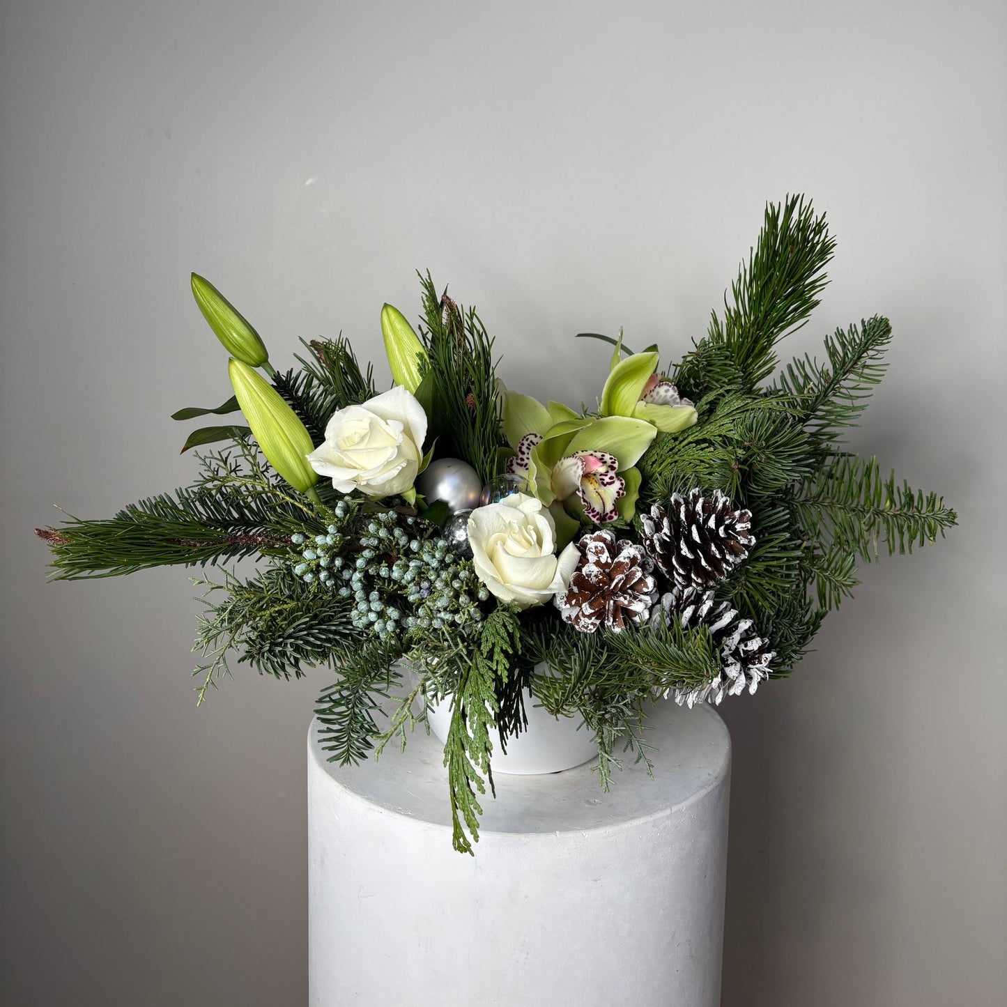 Floral arrangement with greenery, white flowers, and pinecones on a gray background