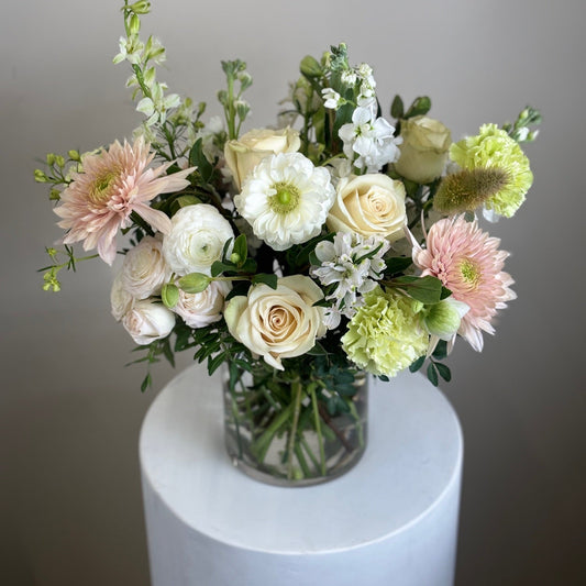 Bouquet of flowers in a clear vase on a white pedestal against a gray background