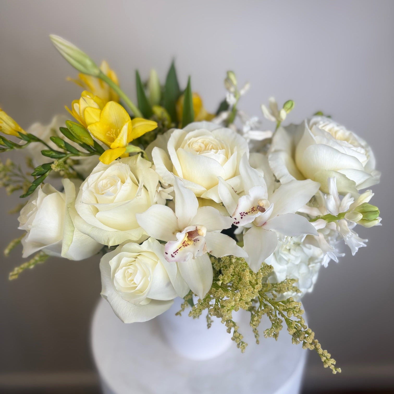 Floral arrangement with white and yellow flowers in a white vase on a neutral background