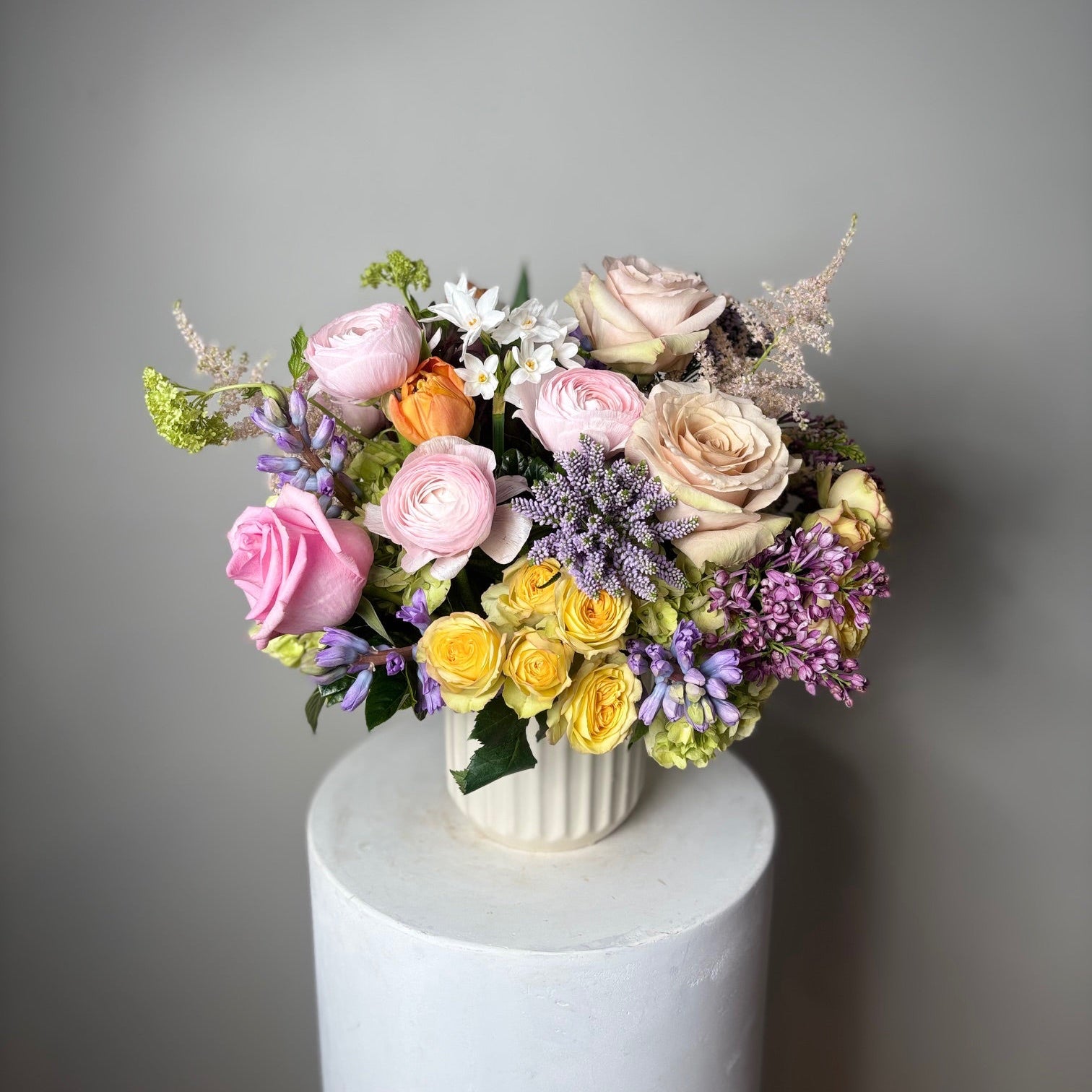 Colorful flower arrangement in a vase on a white pedestal against a gray background