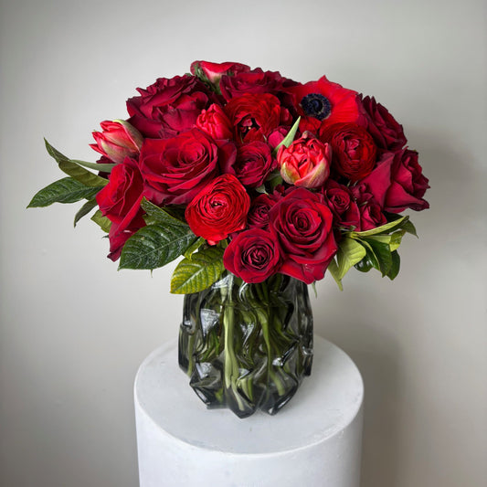 Bouquet of red roses with green leaves in a white vase on a light gray background