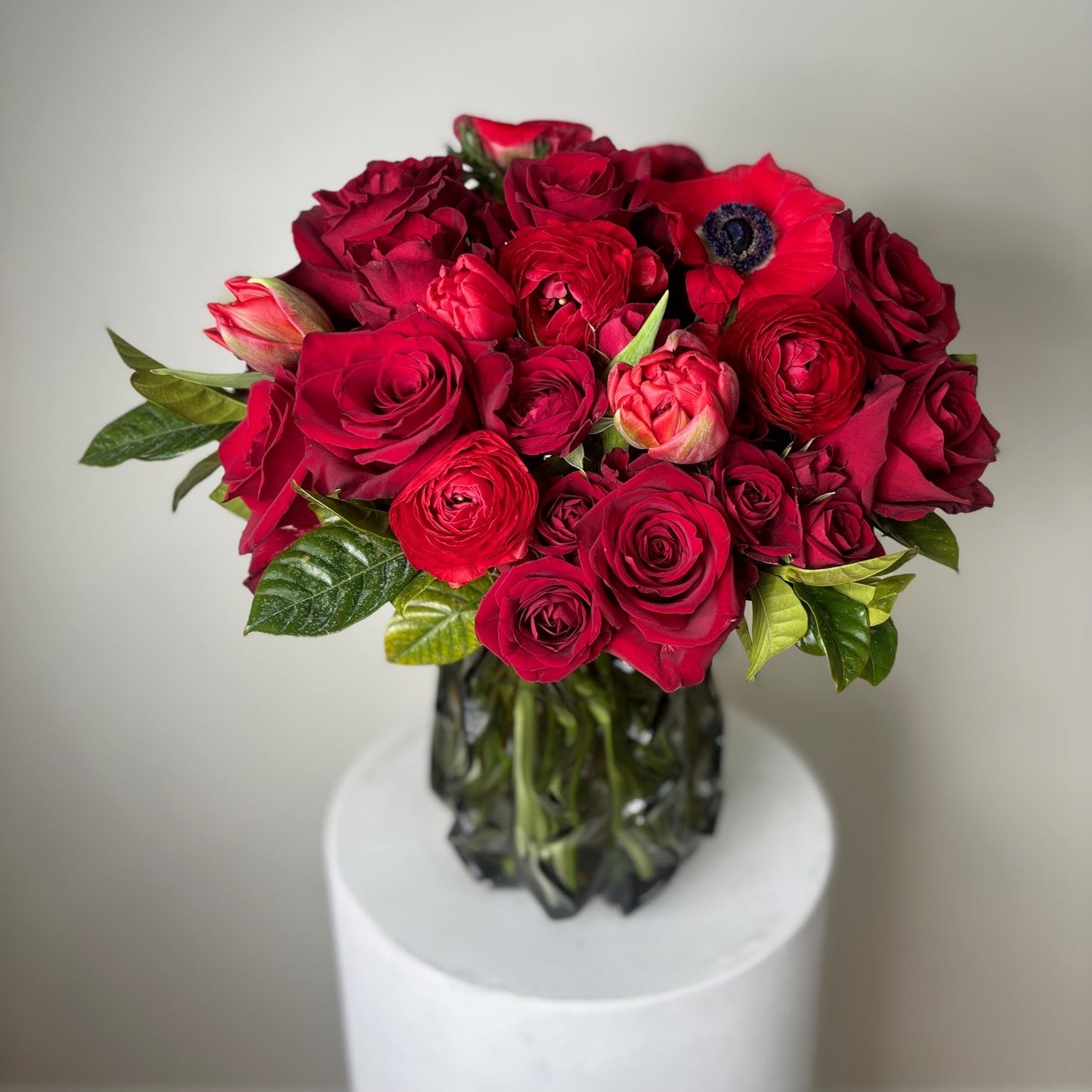 Bouquet of red flowers in a clear vase on a white pedestal against a plain background