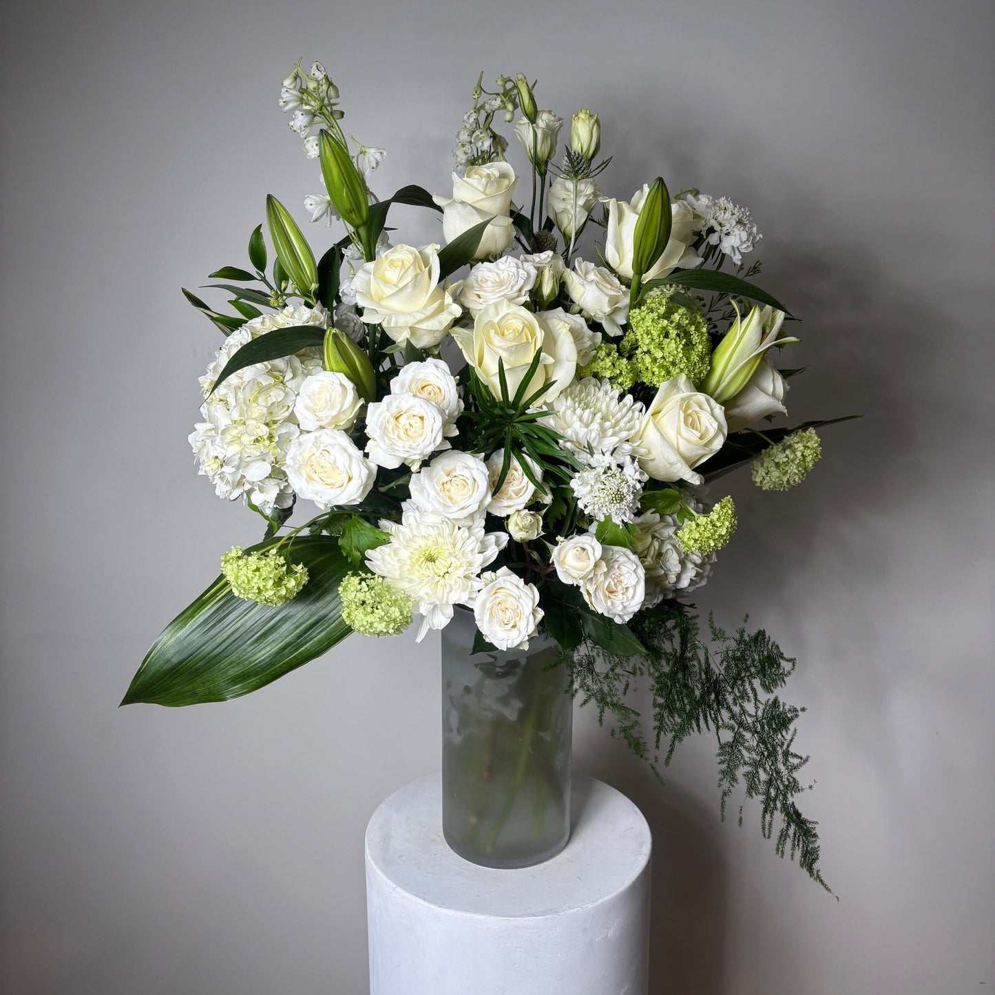 Bouquet of white and green flowers in a clear vase on a gray background