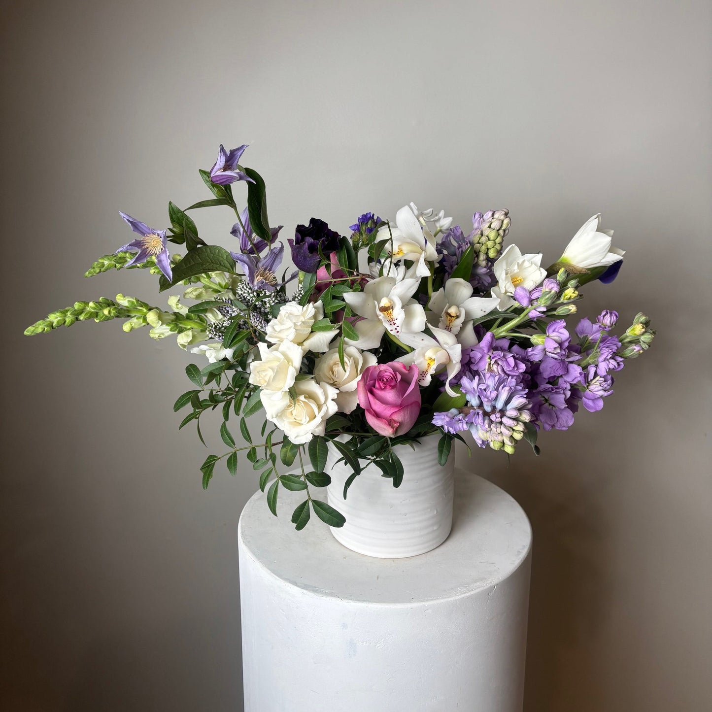 Violet Flower Arrangement in a vase on neutral background with flowers like orchid, roses, stock 
