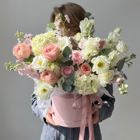 Person holding a large bouquet of flowers in a pink container against a gray background