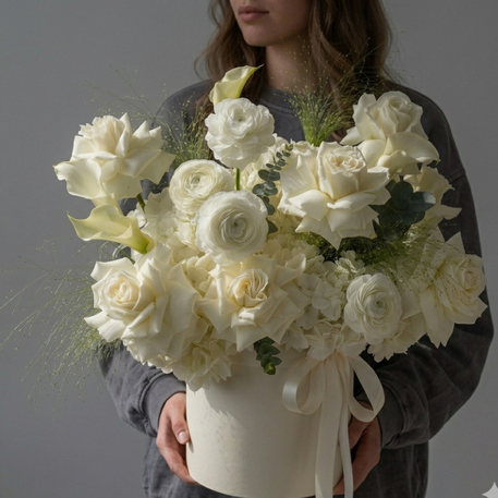 Person holding a bouquet of white flowers in a box against a gray background